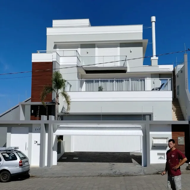 Fachada branca e cinza de uma residência, com varandas e portão.