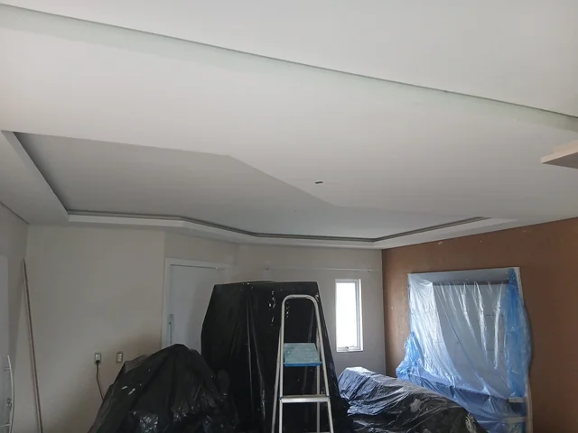 Teto com rebaixo em ambiente em obra, com móveis protegidos.