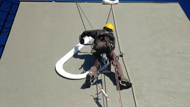 Registro de profissional suspenso por cordas trabalhando em uma parede externa.