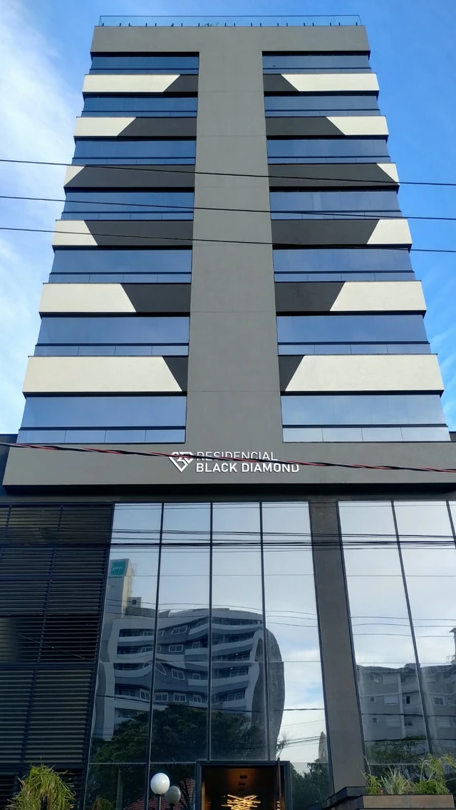 Vista frontal do edifício, com acabamento cinza, faixas claras e entrada de vidro.