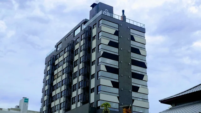 Edifício de esquina com fachada cinza, varandas e janelas.