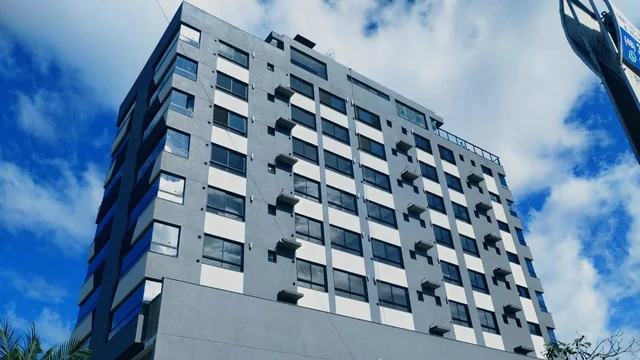 Edifício com fachada clara e cinza, visto de baixo sob o céu azul.