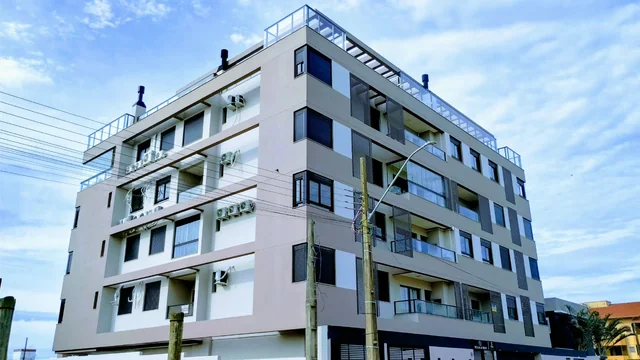 Edifício residencial de fachada clara e cinza, visto da esquina.