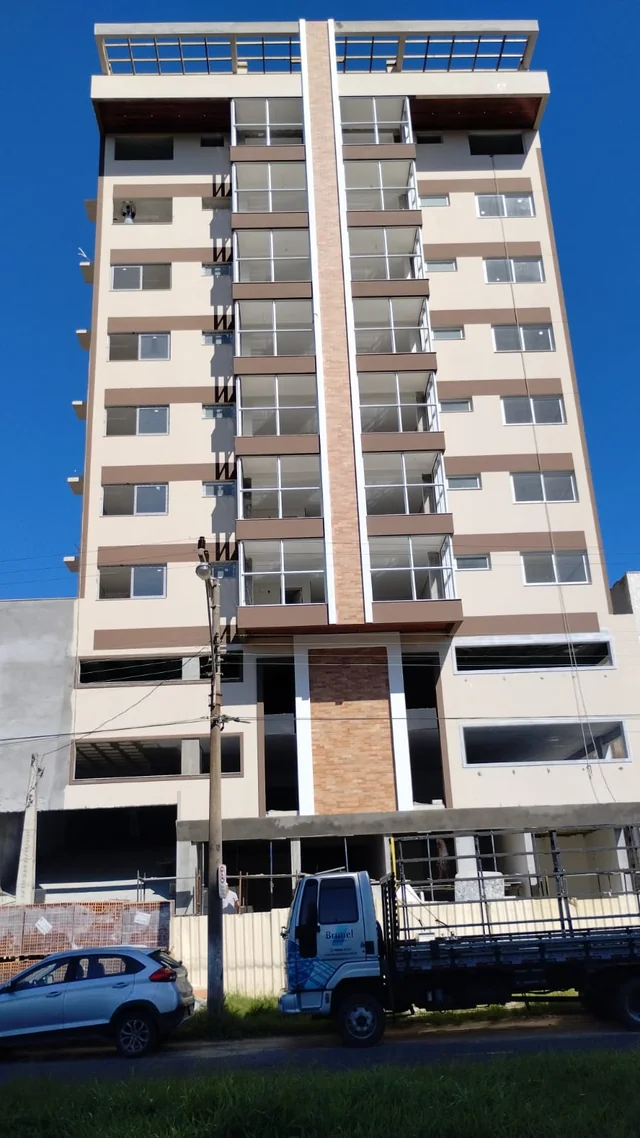 Vista frontal de edifício com varandas e pintura em tons claros e cinza.