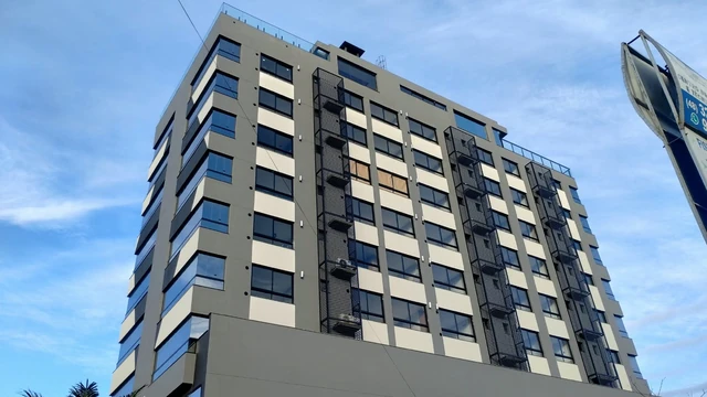Fachada de edifício em tons de cinza, com janelas e detalhes verticais, vista de baixo em perspectiva.