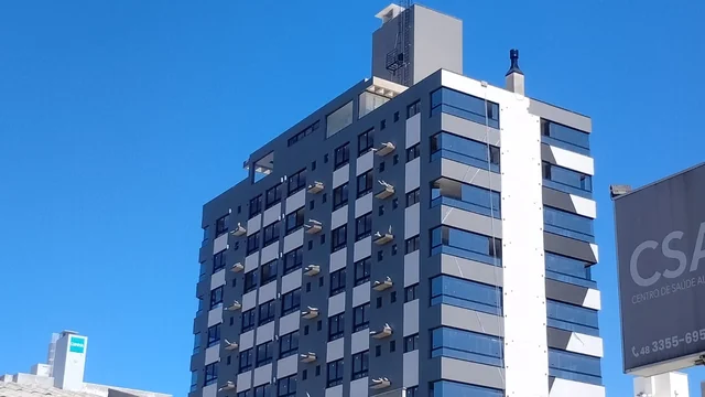 Edifício de fachada cinza e azul visto da rua, com céu azul ao fundo.