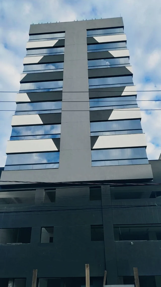Vista frontal de edifício com fachada cinza e janelas envidraçadas.