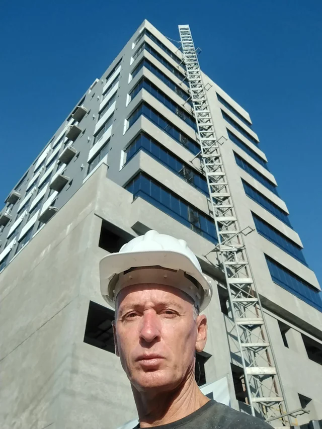 Profissional de capacete em primeiro plano, diante de um edifício.