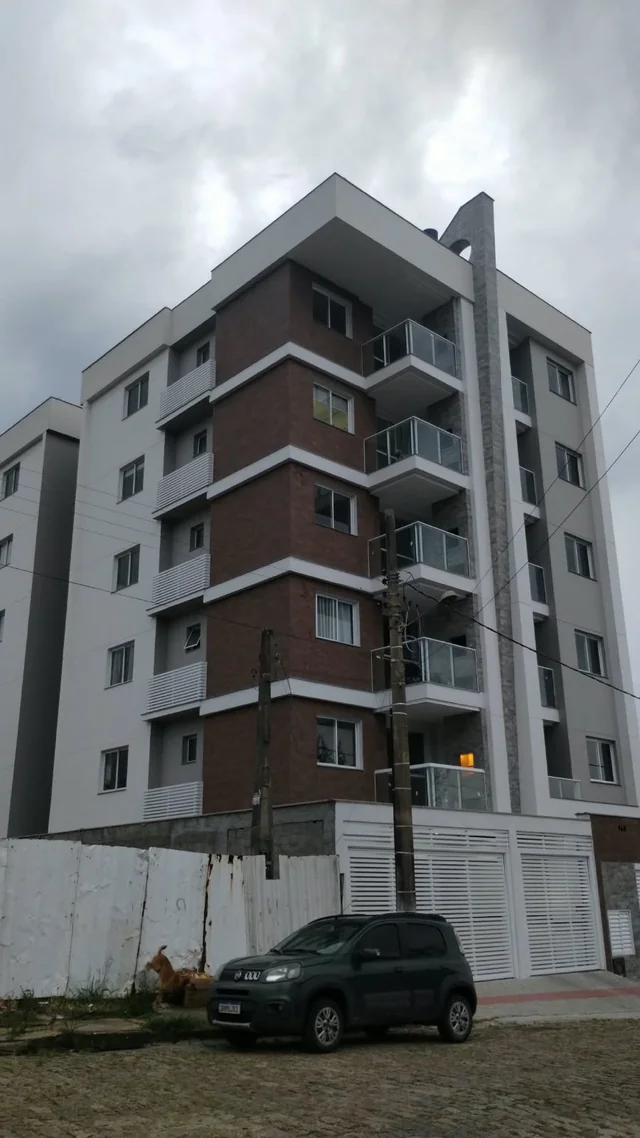 Edifício residencial com varandas e fachada em tons claros, cinza e marrom.